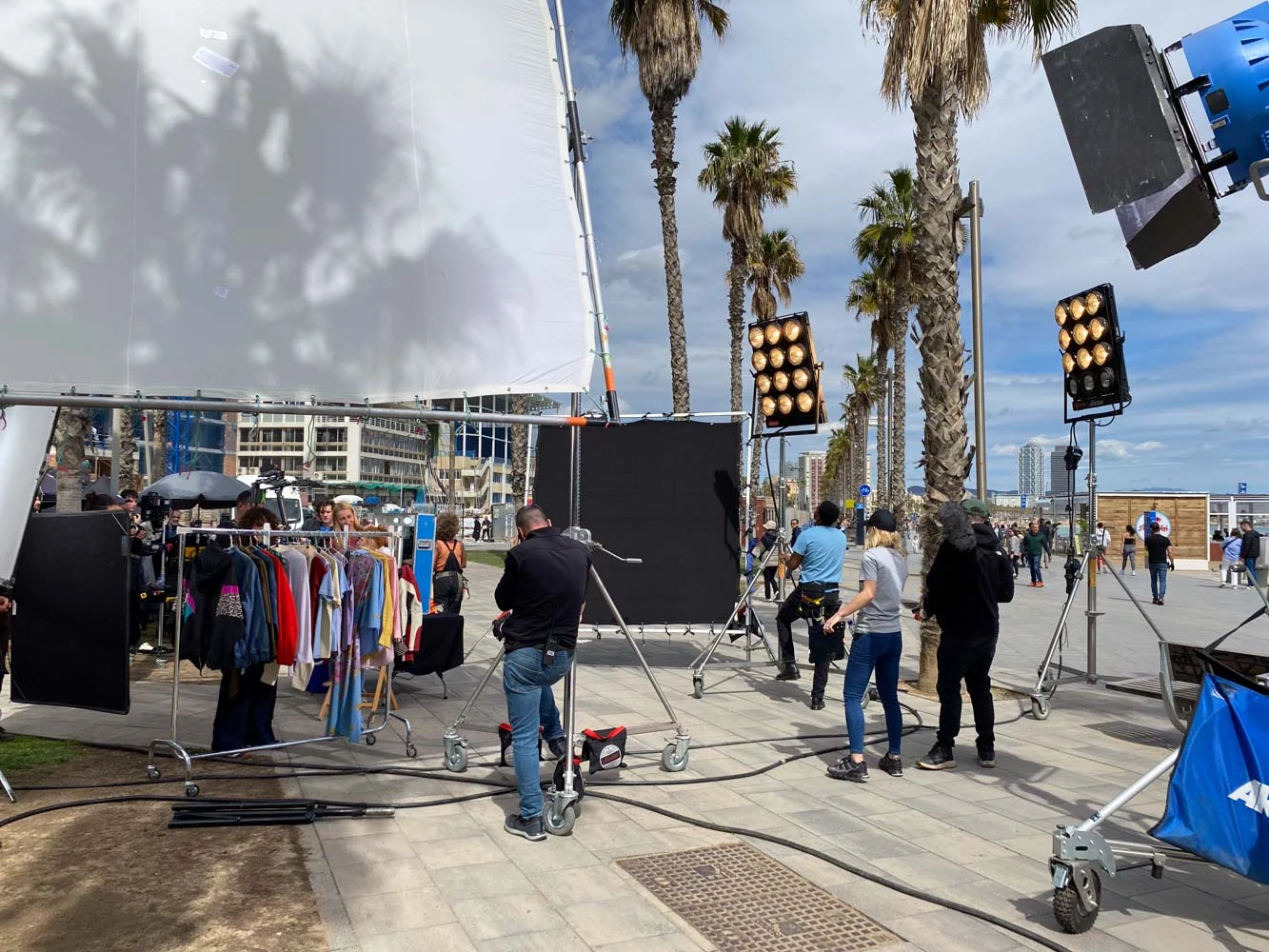 DotFive crew with lights, diffusion frames and a wardrobe rack on a palm-lined seafront